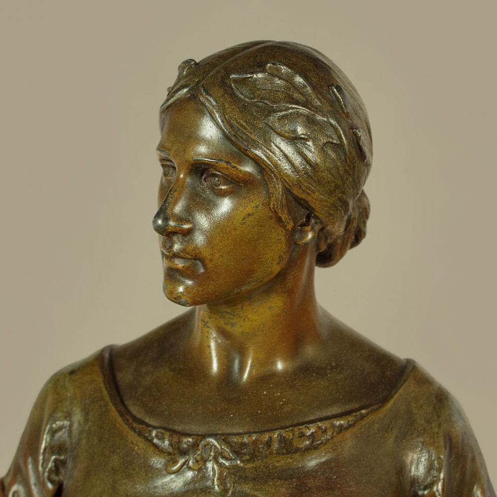 A patinated spelter statue of a standing female figure titled Dignite holding a sword and foliage branch, mounted on an integral square base. View VIII