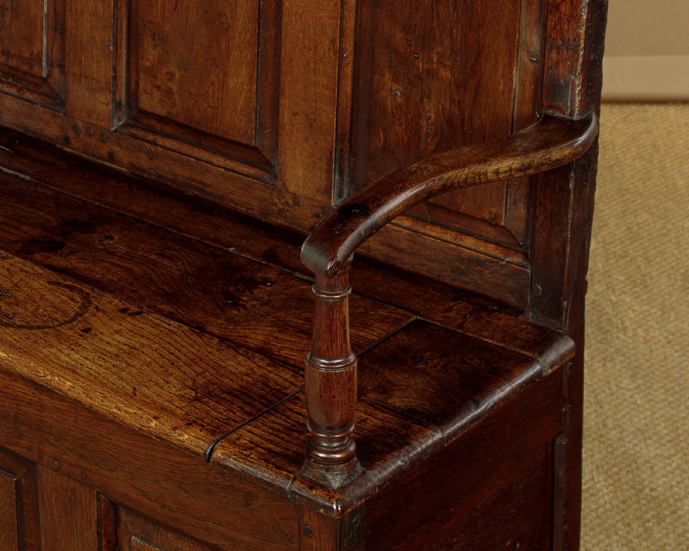 A dark oak box settle featuring a three-panel back with subtle arched top mouldings, curved armrests on turned supports, and a hinged seat opening to storage. View VIII