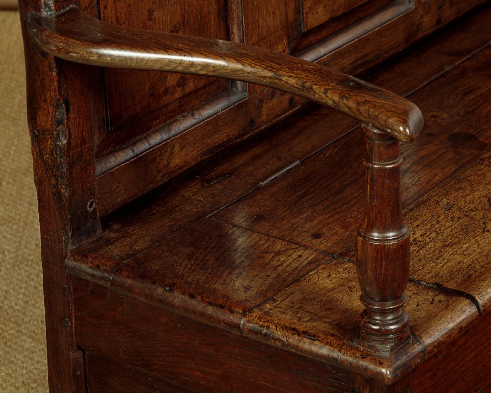 A dark oak box settle featuring a three-panel back with subtle arched top mouldings, curved armrests on turned supports, and a hinged seat opening to storage. View IX