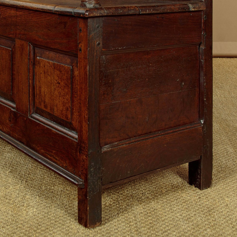 A dark oak box settle featuring a three-panel back with subtle arched top mouldings, curved armrests on turned supports, and a hinged seat opening to storage. View XI