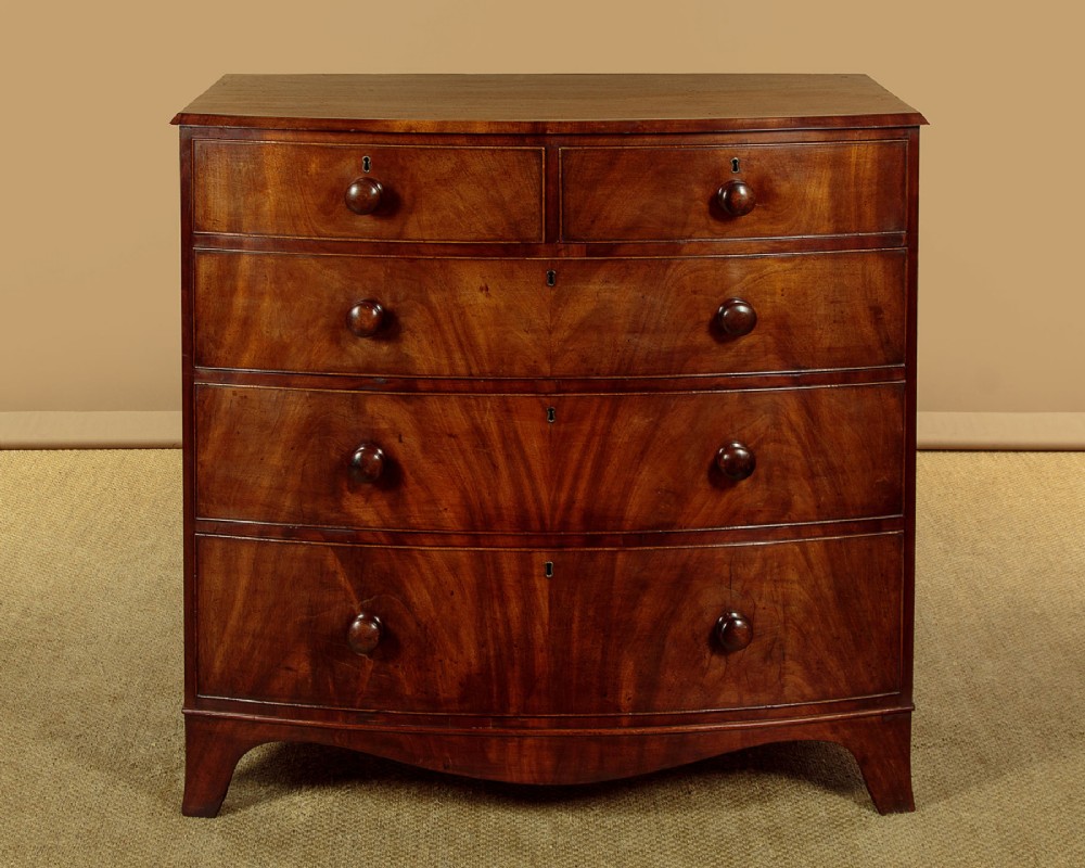 A Regency bowfront mahogany chest of drawers featuring two short and three long drawers with turned wooden knobs and a curved lower apron on splayed feet.