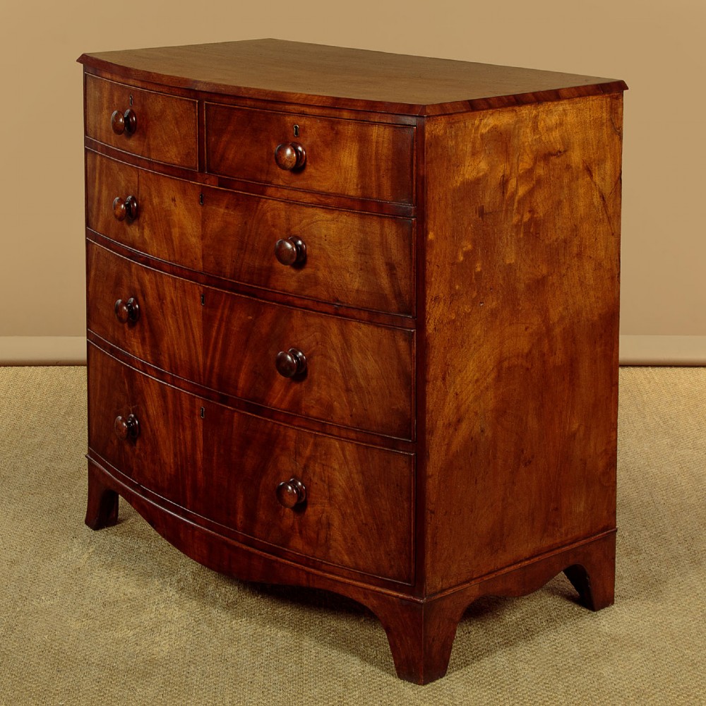 A Regency bowfront mahogany chest of drawers featuring two short and three long drawers with turned wooden knobs and a curved lower apron on splayed feet. View II