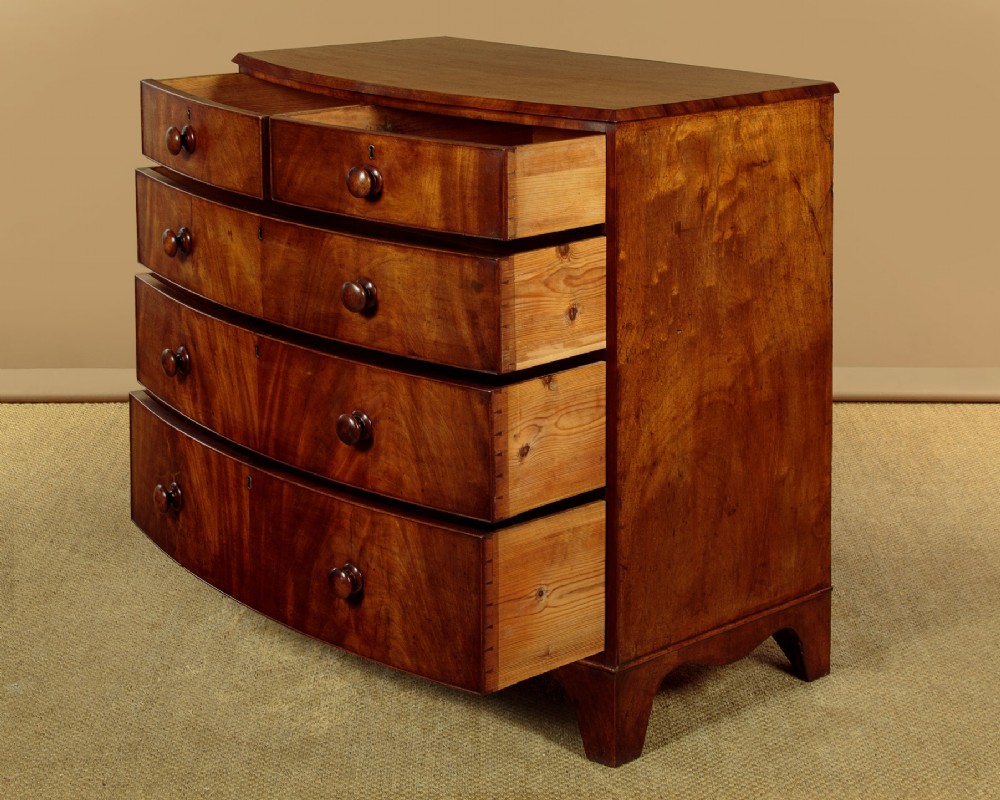 A Regency bowfront mahogany chest of drawers featuring two short and three long drawers with turned wooden knobs and a curved lower apron on splayed feet. View IV