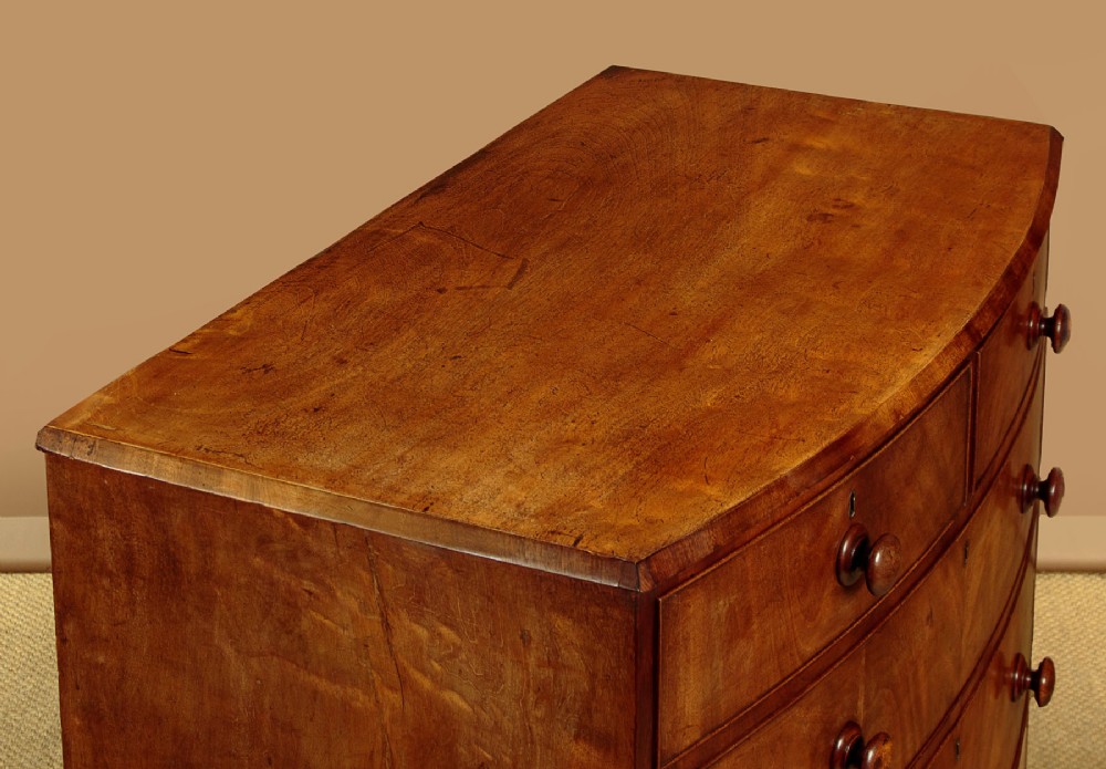 A Regency bowfront mahogany chest of drawers featuring two short and three long drawers with turned wooden knobs and a curved lower apron on splayed feet. View V