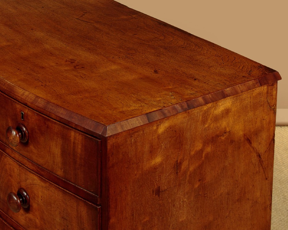 A Regency bowfront mahogany chest of drawers featuring two short and three long drawers with turned wooden knobs and a curved lower apron on splayed feet. View VI