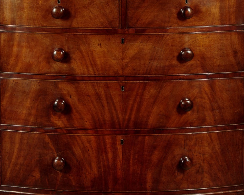 A Regency bowfront mahogany chest of drawers featuring two short and three long drawers with turned wooden knobs and a curved lower apron on splayed feet. View VII