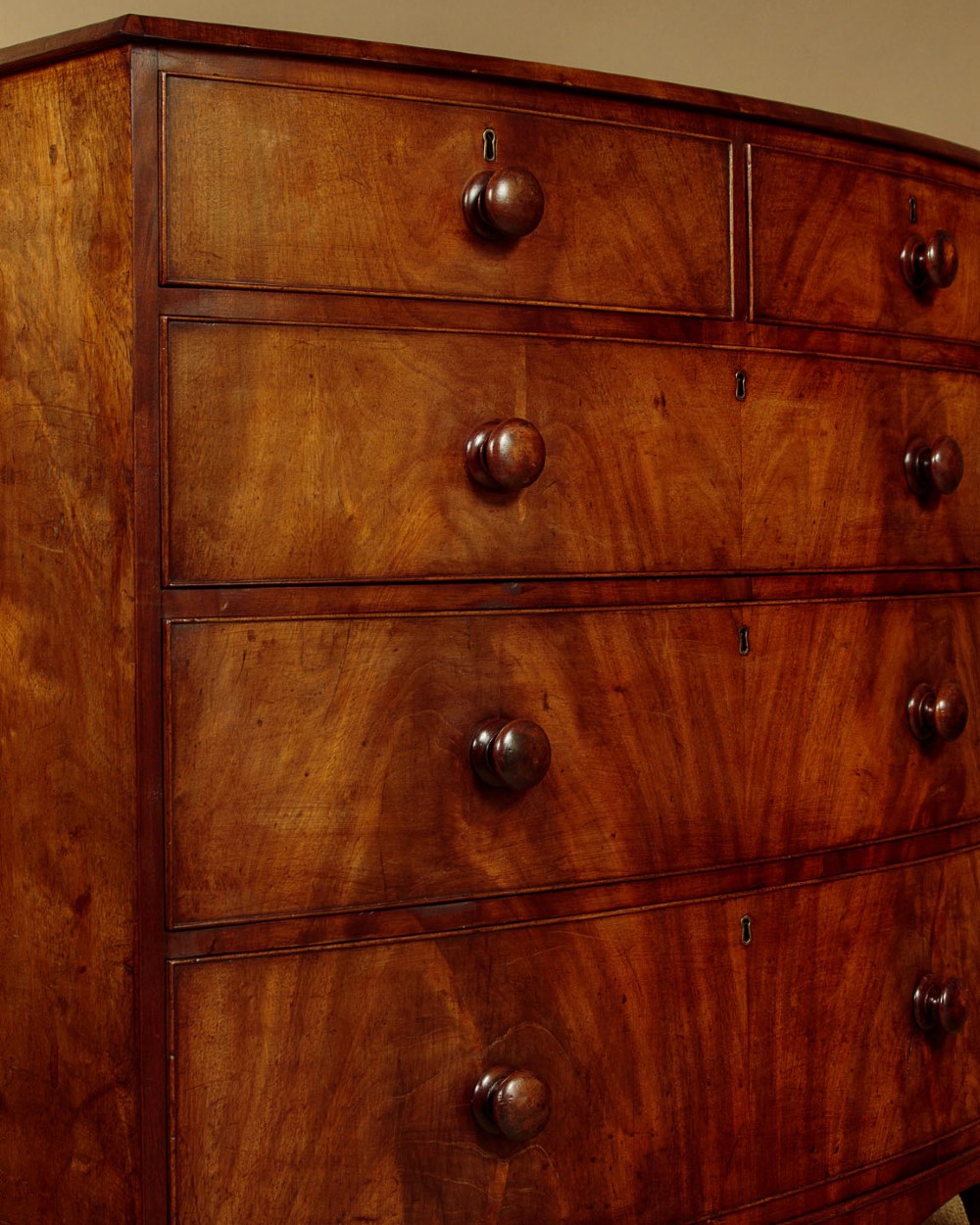 A Regency bowfront mahogany chest of drawers featuring two short and three long drawers with turned wooden knobs and a curved lower apron on splayed feet. View VIII