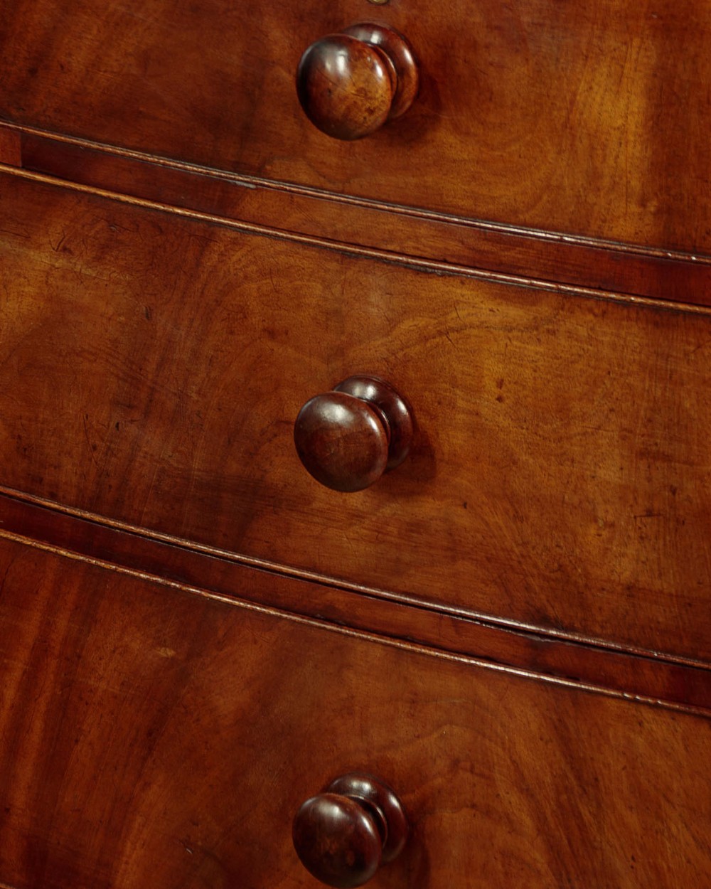 A Regency bowfront mahogany chest of drawers featuring two short and three long drawers with turned wooden knobs and a curved lower apron on splayed feet. View IX