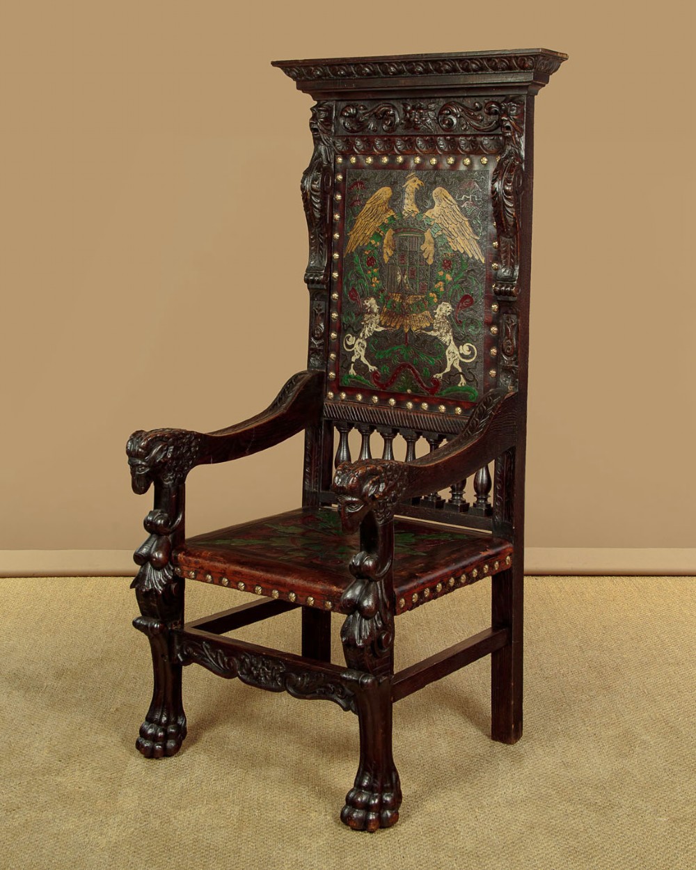 A tall, dark carved oak Renaissance Revival throne chair featuring a high back with a painted heraldic leather panel, lion head terminal armrests, and brass stud trim.