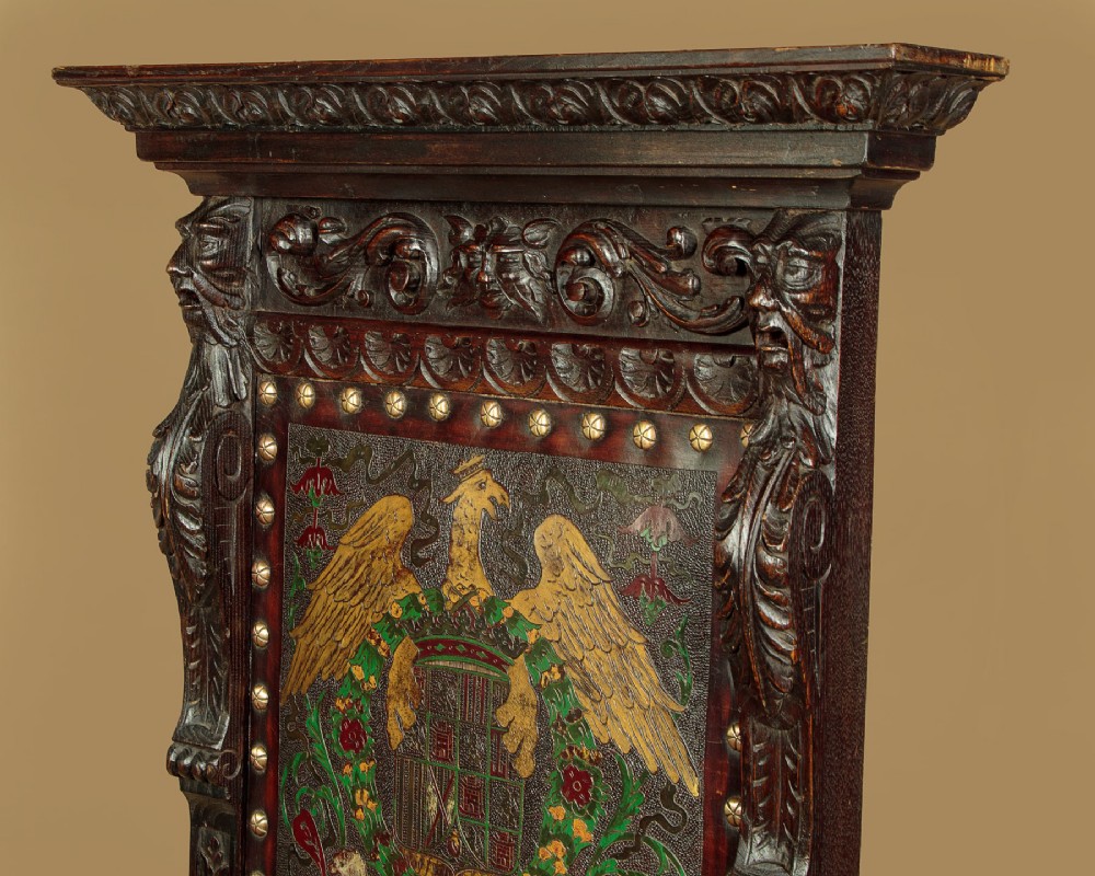 A tall, dark carved oak Renaissance Revival throne chair featuring a high back with a painted heraldic leather panel, lion head terminal armrests, and brass stud trim. View IV