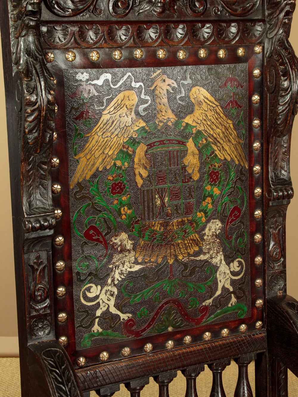 A tall, dark carved oak Renaissance Revival throne chair featuring a high back with a painted heraldic leather panel, lion head terminal armrests, and brass stud trim. View V