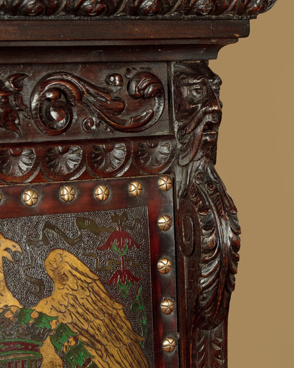 A tall, dark carved oak Renaissance Revival throne chair featuring a high back with a painted heraldic leather panel, lion head terminal armrests, and brass stud trim. View VI