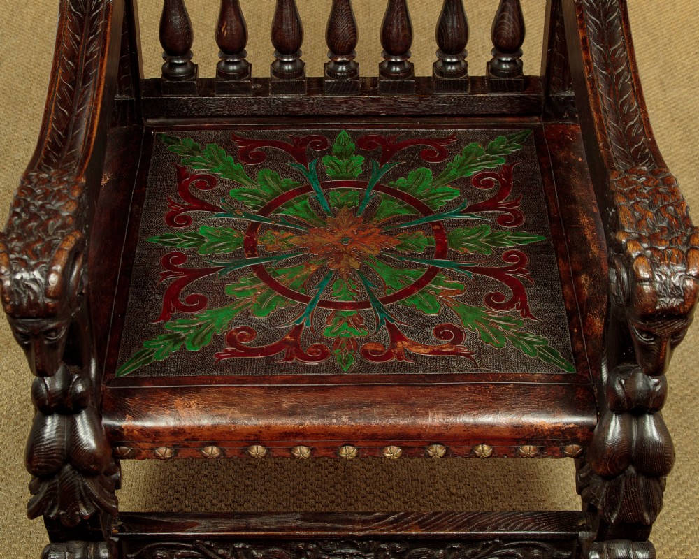 A tall, dark carved oak Renaissance Revival throne chair featuring a high back with a painted heraldic leather panel, lion head terminal armrests, and brass stud trim. View VII
