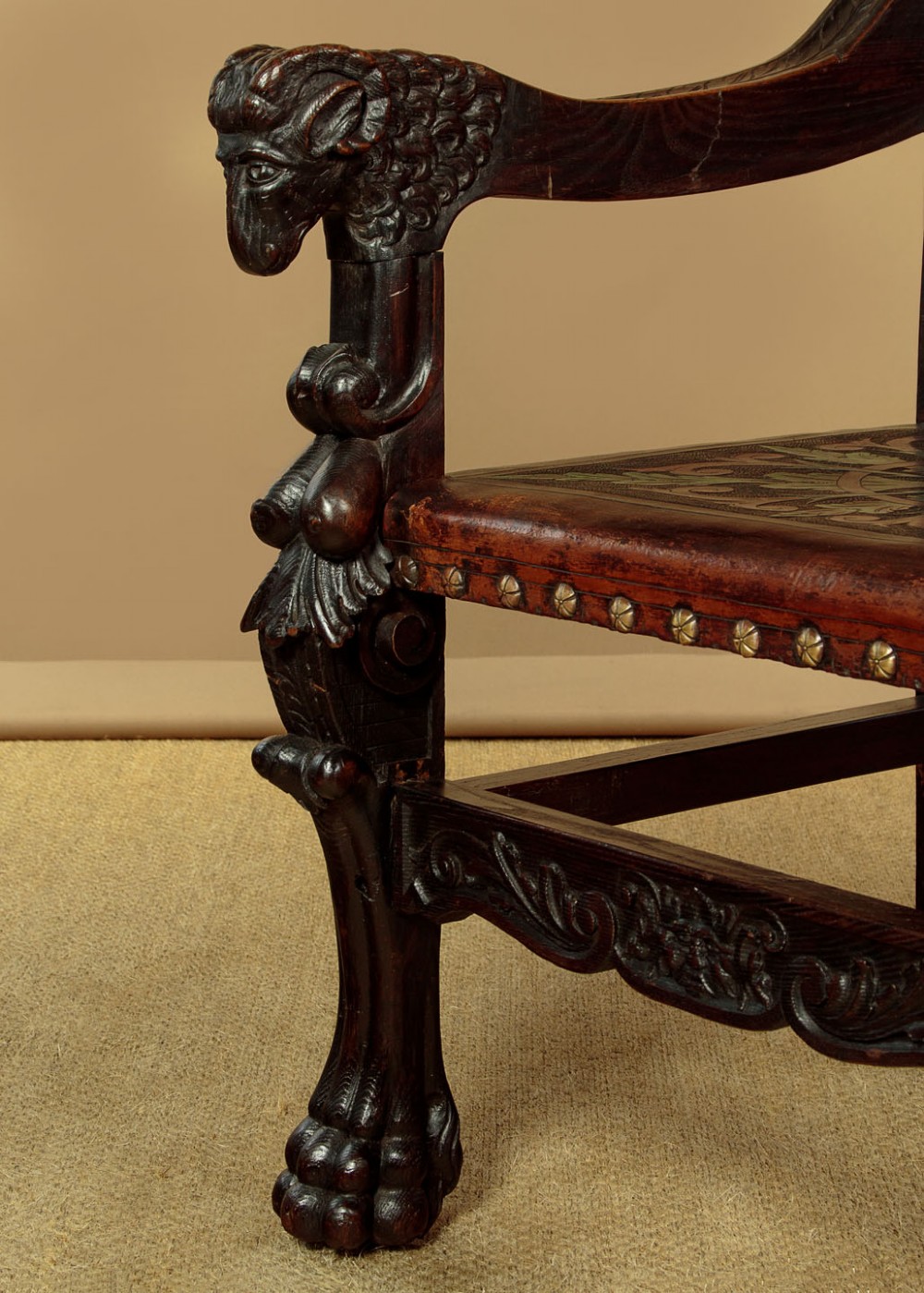 A tall, dark carved oak Renaissance Revival throne chair featuring a high back with a painted heraldic leather panel, lion head terminal armrests, and brass stud trim. View VIII