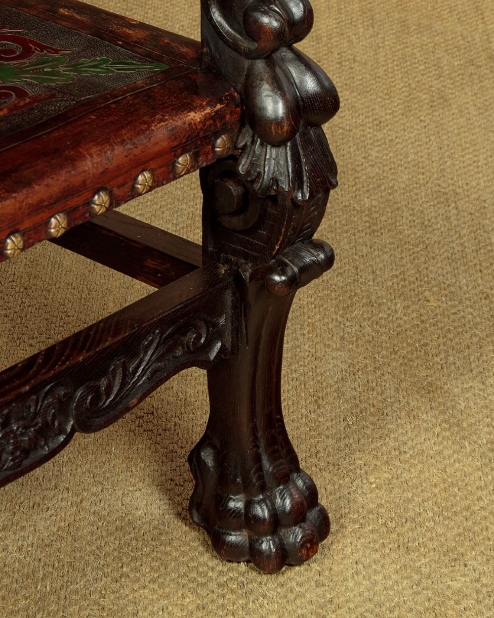A tall, dark carved oak Renaissance Revival throne chair featuring a high back with a painted heraldic leather panel, lion head terminal armrests, and brass stud trim. View X