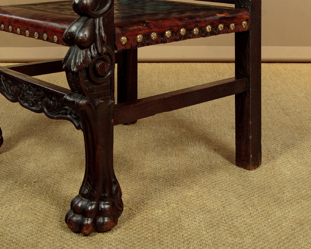 A tall, dark carved oak Renaissance Revival throne chair featuring a high back with a painted heraldic leather panel, lion head terminal armrests, and brass stud trim. View XI