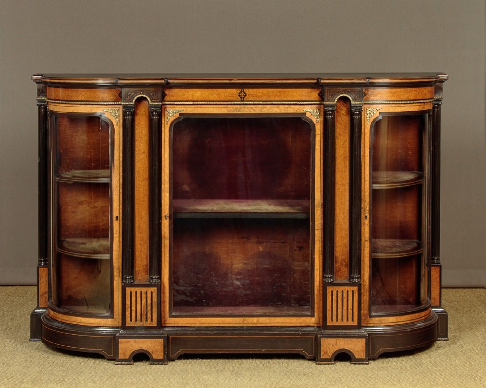 A late Victorian ebonised and burr walnut credenza featuring a central glazed door flanked by two curved side display glass doors with fluted column supports.