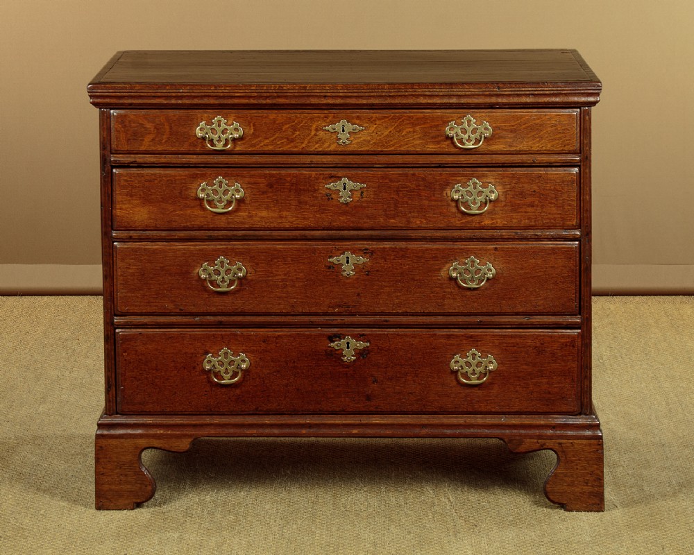 A Georgian oak chest of drawers featuring four graduated drawers with decorative pierced brass handles and bracket feet.
