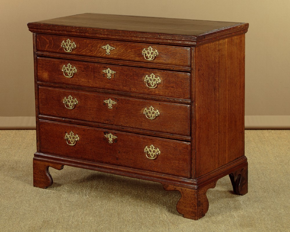 A Georgian oak chest of drawers featuring four graduated drawers with decorative pierced brass handles and bracket feet. View II