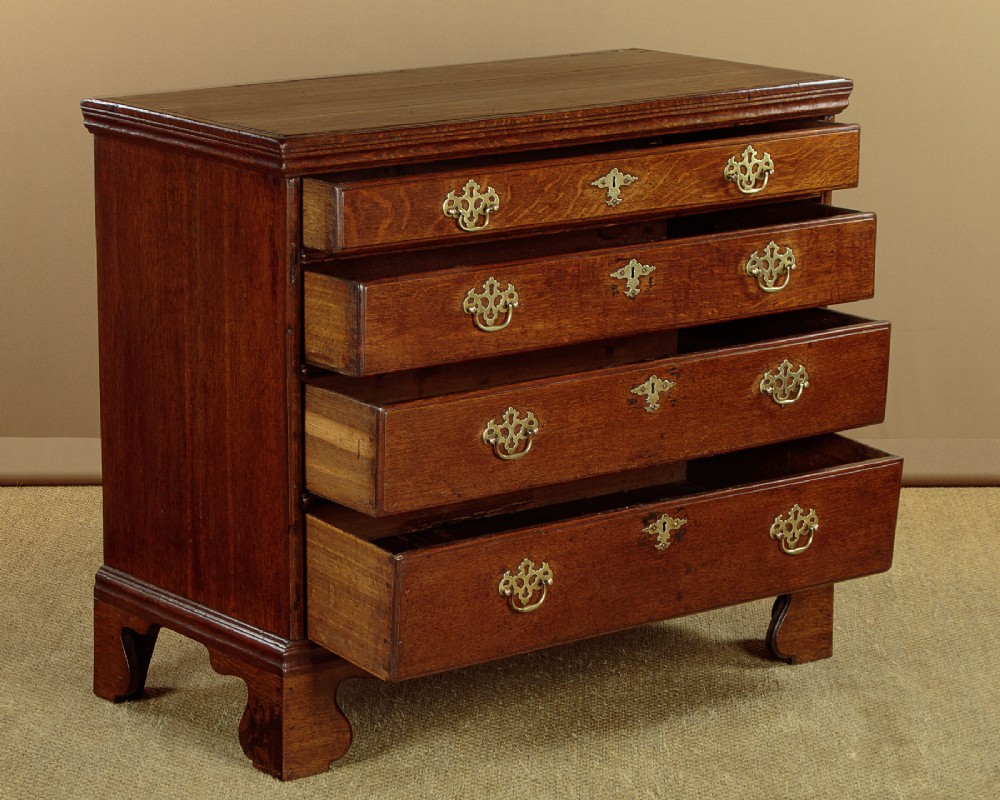 A Georgian oak chest of drawers featuring four graduated drawers with decorative pierced brass handles and bracket feet. View III