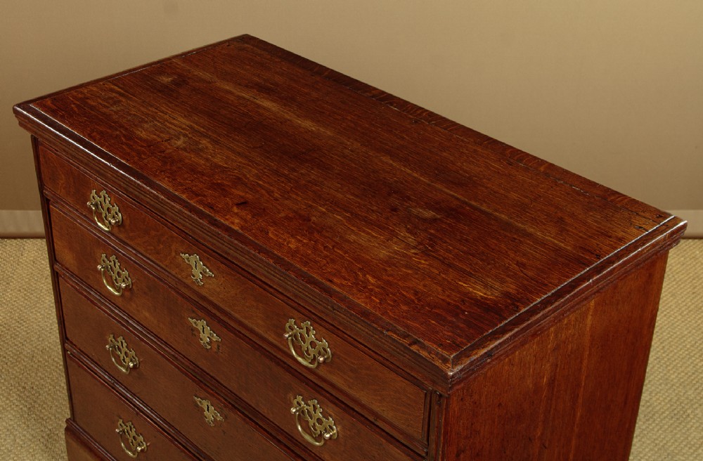 A Georgian oak chest of drawers featuring four graduated drawers with decorative pierced brass handles and bracket feet. View IV