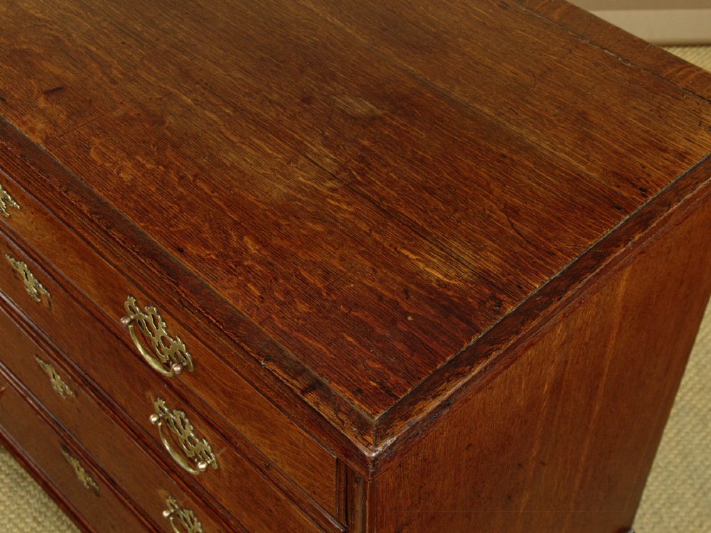 A Georgian oak chest of drawers featuring four graduated drawers with decorative pierced brass handles and bracket feet. View V