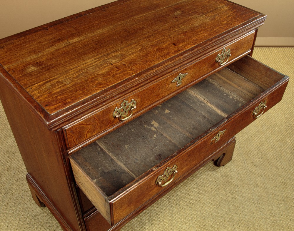 A Georgian oak chest of drawers featuring four graduated drawers with decorative pierced brass handles and bracket feet. View VI