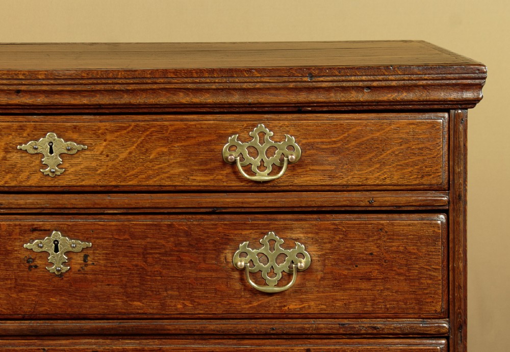 A Georgian oak chest of drawers featuring four graduated drawers with decorative pierced brass handles and bracket feet. View VII