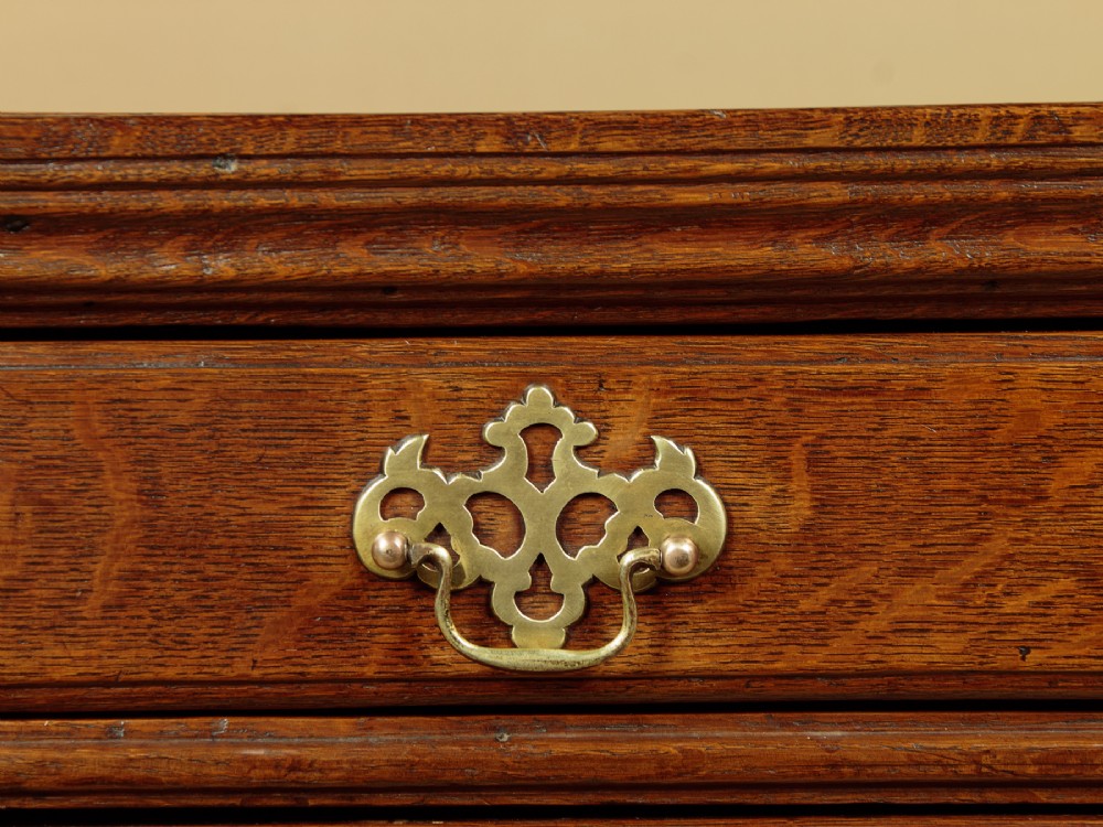 A Georgian oak chest of drawers featuring four graduated drawers with decorative pierced brass handles and bracket feet. View VIII
