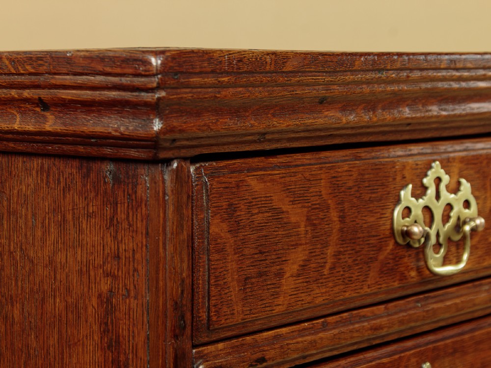 A Georgian oak chest of drawers featuring four graduated drawers with decorative pierced brass handles and bracket feet. View IX