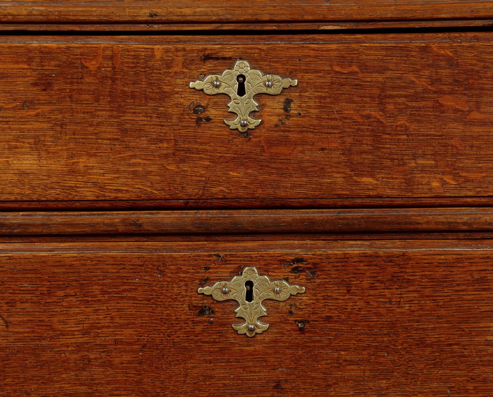 A Georgian oak chest of drawers featuring four graduated drawers with decorative pierced brass handles and bracket feet. View X