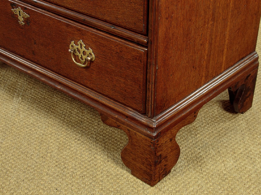 A Georgian oak chest of drawers featuring four graduated drawers with decorative pierced brass handles and bracket feet. View XI
