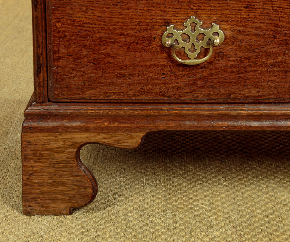 A Georgian oak chest of drawers featuring four graduated drawers with decorative pierced brass handles and bracket feet. View XII