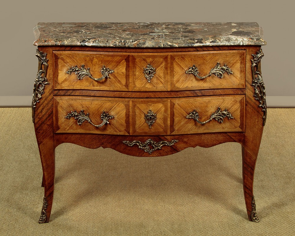 A 1930s Louis XV style bombe commode featuring a variegated grey marble top, parquetry wood veneer drawers, and ornate brass mounts.