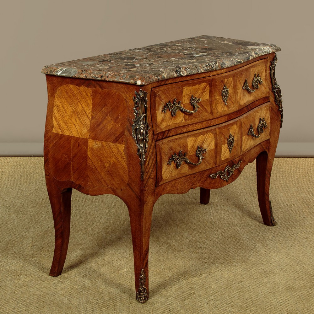 A 1930s Louis XV style bombe commode featuring a variegated grey marble top, parquetry wood veneer drawers, and ornate brass mounts. View II