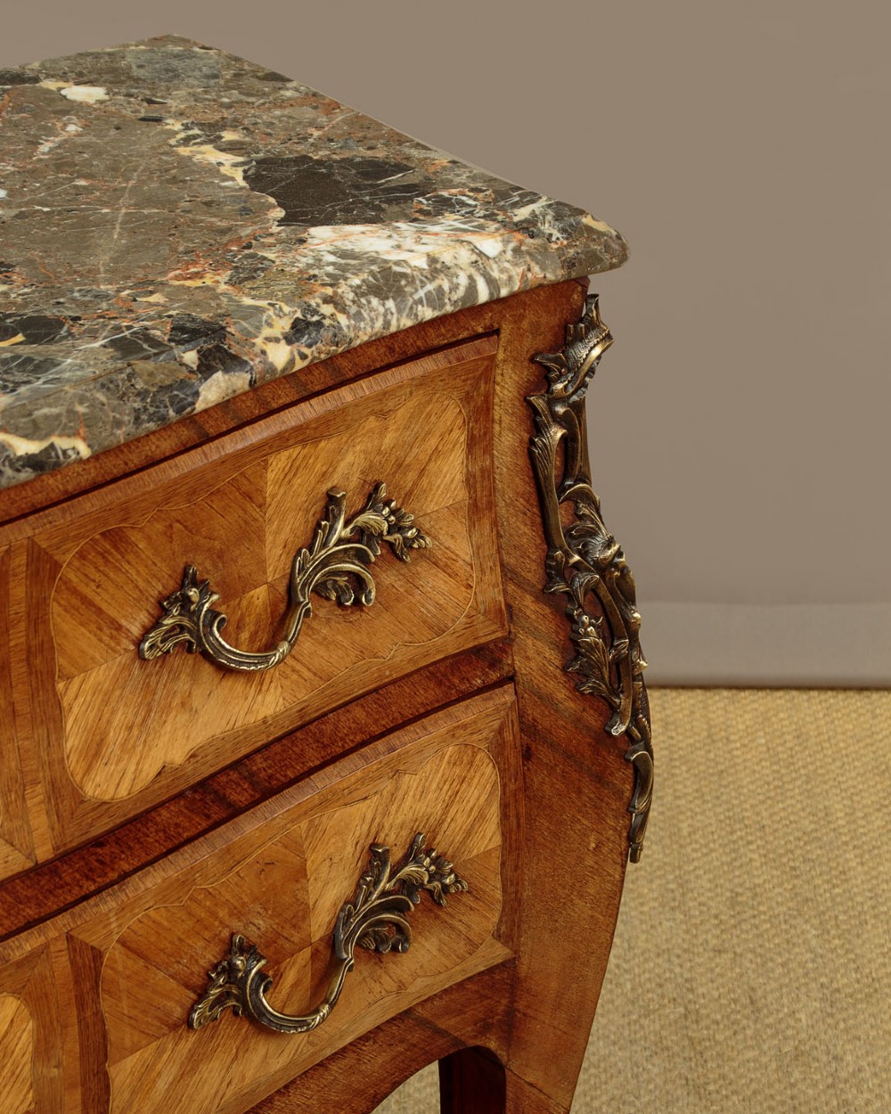 A 1930s Louis XV style bombe commode featuring a variegated grey marble top, parquetry wood veneer drawers, and ornate brass mounts. View IX
