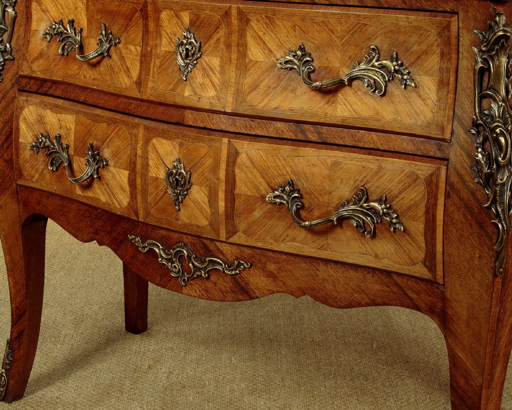 A 1930s Louis XV style bombe commode featuring a variegated grey marble top, parquetry wood veneer drawers, and ornate brass mounts. View X