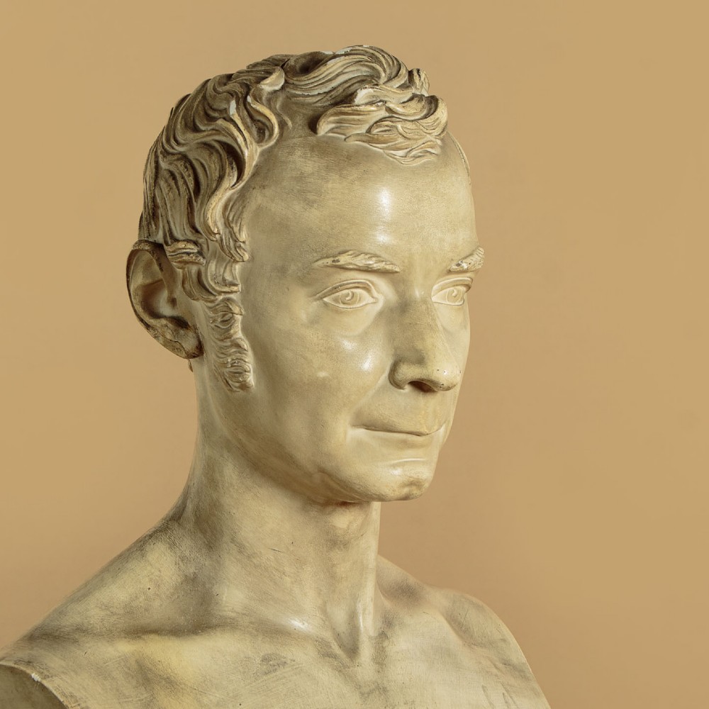 An off-white mid-nineteenth-century plaster bust depicting a gentleman with short wavy hair and bare shoulders. View IV