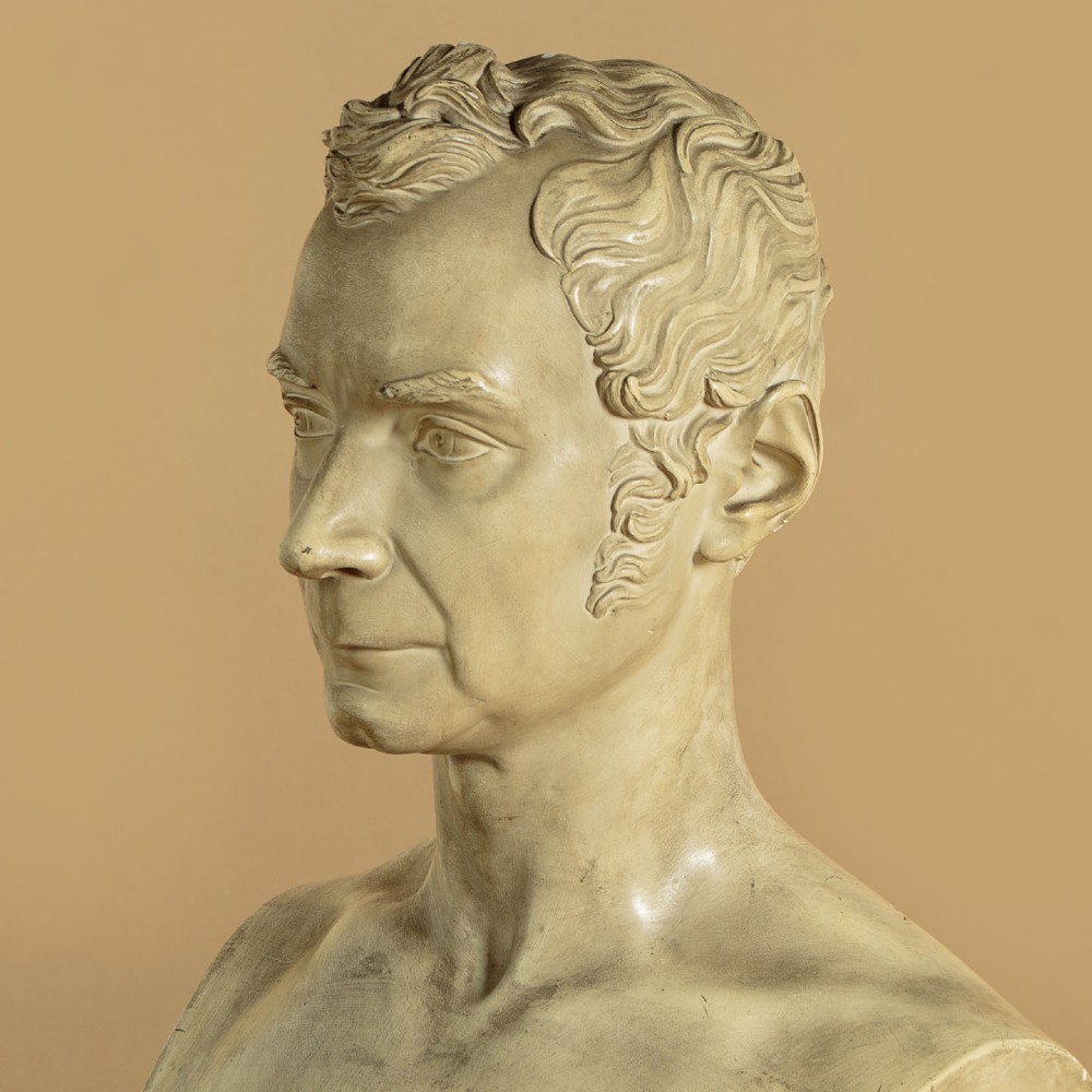 An off-white mid-nineteenth-century plaster bust depicting a gentleman with short wavy hair and bare shoulders. View V