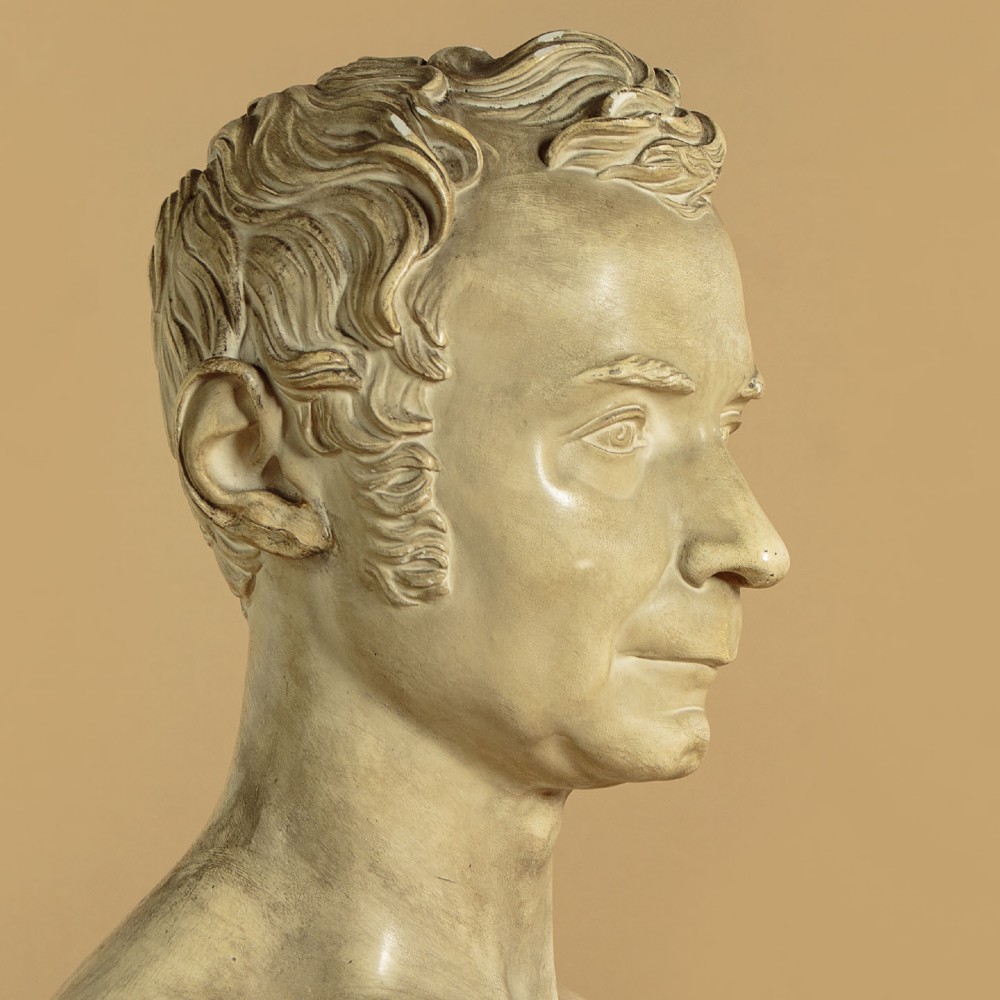An off-white mid-nineteenth-century plaster bust depicting a gentleman with short wavy hair and bare shoulders. View VI