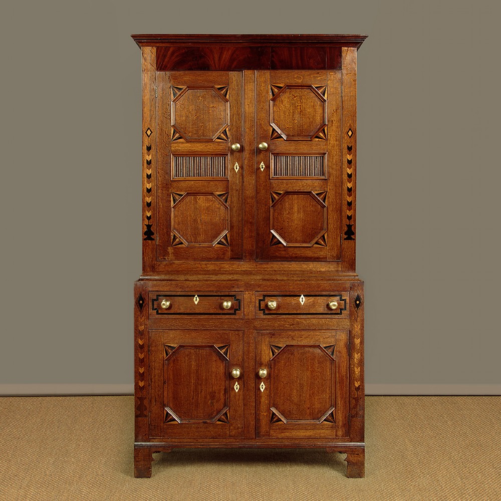 An antique 19th-century Welsh oak bread and cheese cupboard featuring geometric inlaid border details, upper slatted ventilated doors, two drawers, and lower panelled doors on bracket feet.
