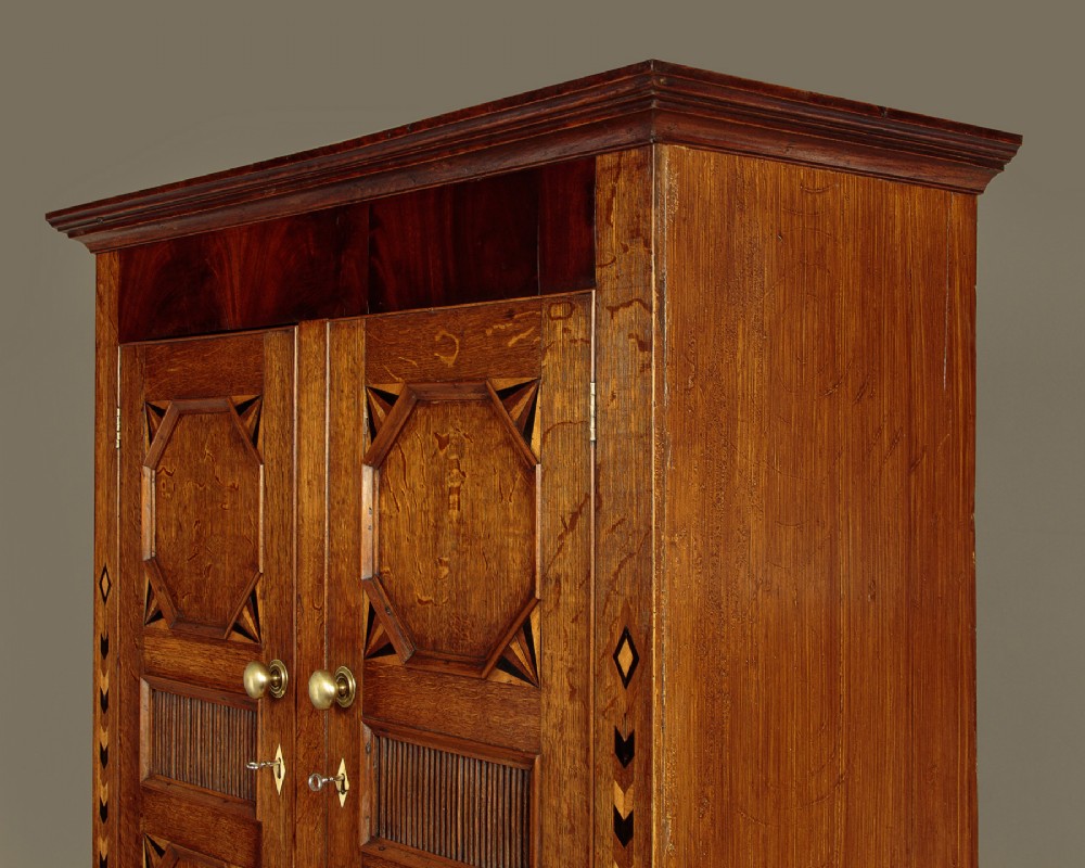 An antique 19th-century Welsh oak bread and cheese cupboard featuring geometric inlaid border details, upper slatted ventilated doors, two drawers, and lower panelled doors on bracket feet. View VI