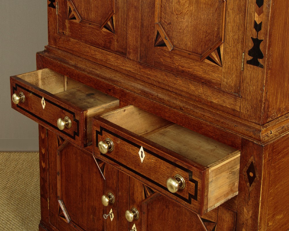 An antique 19th-century Welsh oak bread and cheese cupboard featuring geometric inlaid border details, upper slatted ventilated doors, two drawers, and lower panelled doors on bracket feet. View X