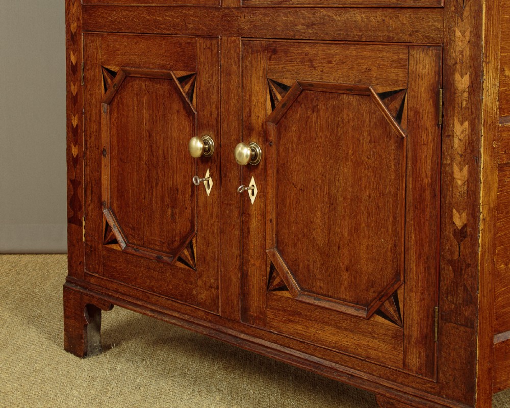 An antique 19th-century Welsh oak bread and cheese cupboard featuring geometric inlaid border details, upper slatted ventilated doors, two drawers, and lower panelled doors on bracket feet. View XIV