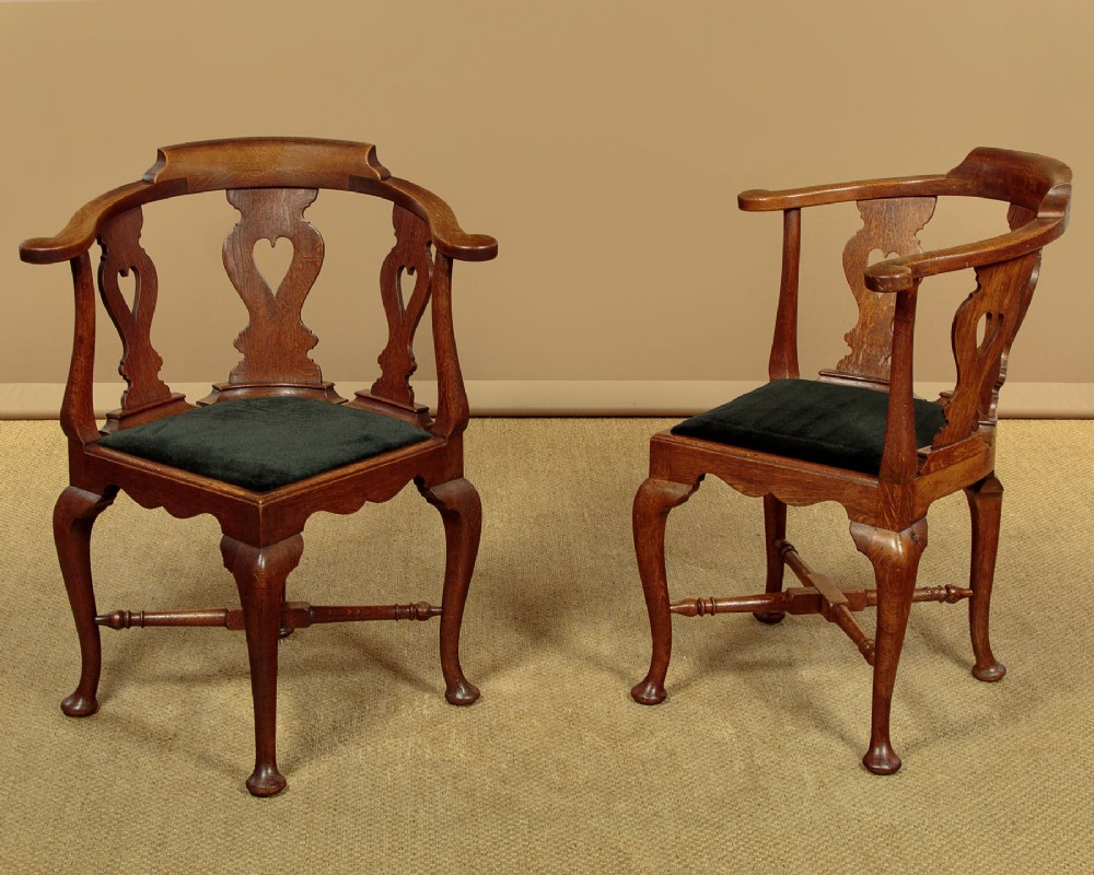 A pair of dark oak corner armchairs featuring pierced heart splats, cabriole legs, turned stretchers, and black upholstered seat cushions. View II