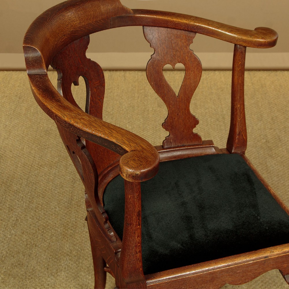 A pair of dark oak corner armchairs featuring pierced heart splats, cabriole legs, turned stretchers, and black upholstered seat cushions. View V