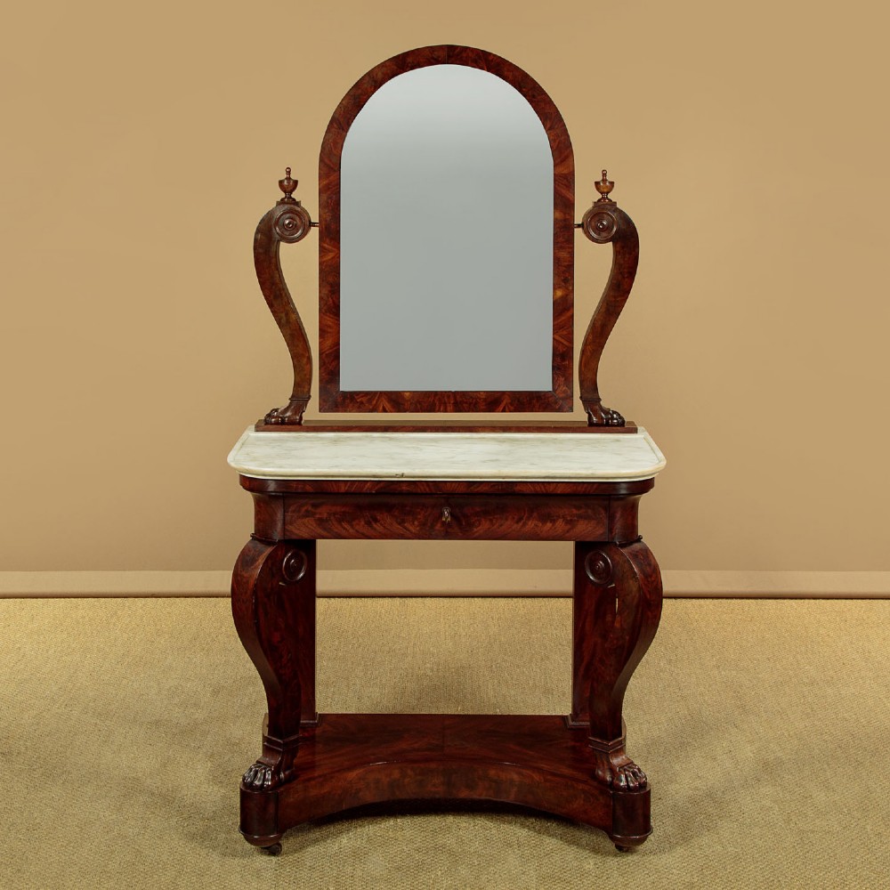 A mid-19th-century mahogany dressing table featuring a white marble surface, arched swing mirror on carved scroll supports, and lower plinth base.