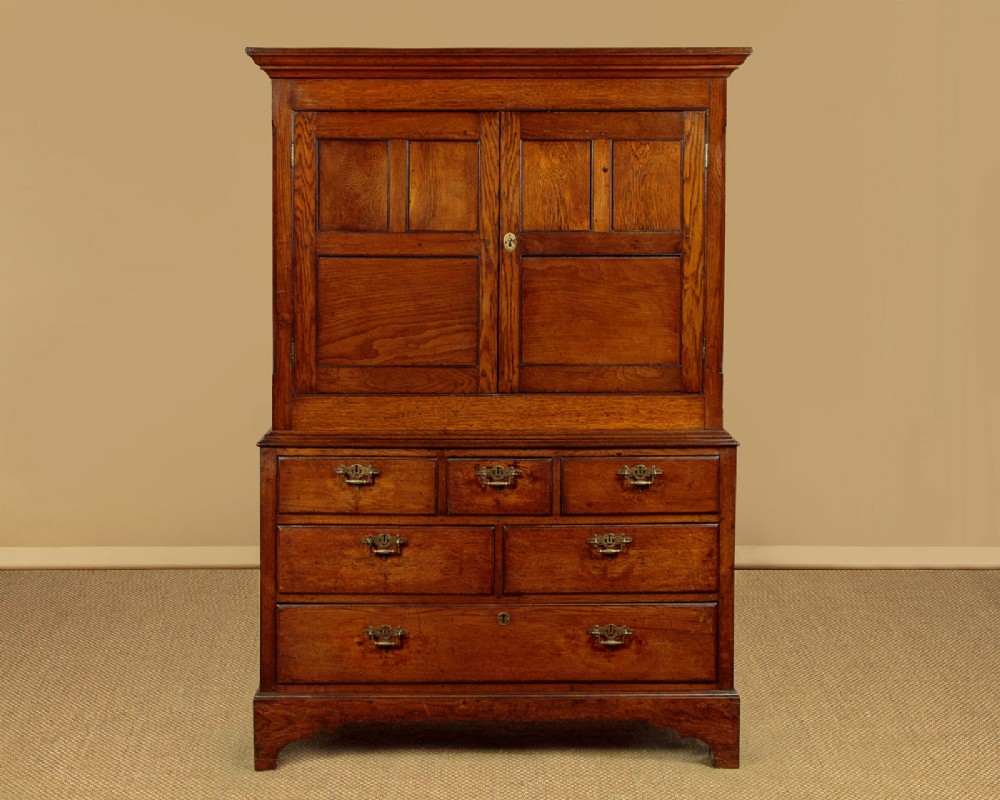 An antique two-part Welsh oak cupboard featuring a double door top section with fielded panels above a chest with six drawers on bracket feet.