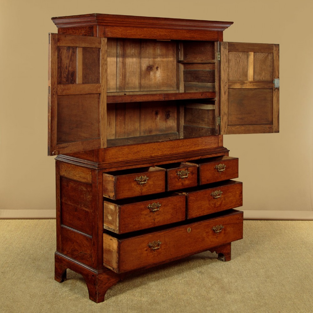 An antique two-part Welsh oak cupboard featuring a double door top section with fielded panels above a chest with six drawers on bracket feet. View V