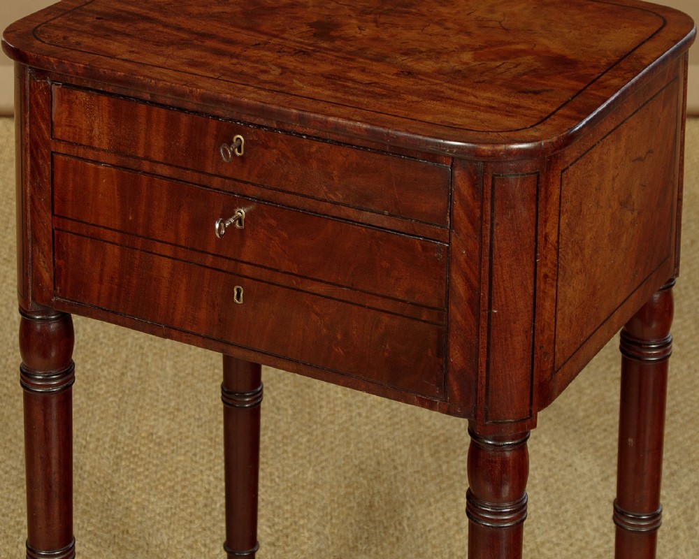 A George III mahogany side table featuring three shallow drawers, ring-turned legs on brass castors, and a rich wood grain finish. View VIII